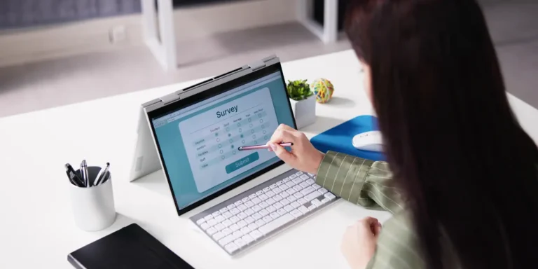 A woman focused on her laptop, seated at a desk with a notepad and pen nearby.