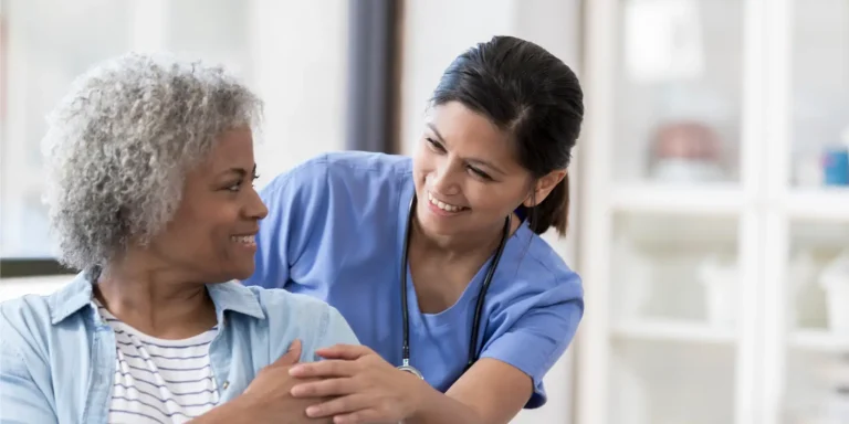 A smiling nurse stands beside an elderly woman, highlighting a moment of compassion and connection in healthcare.