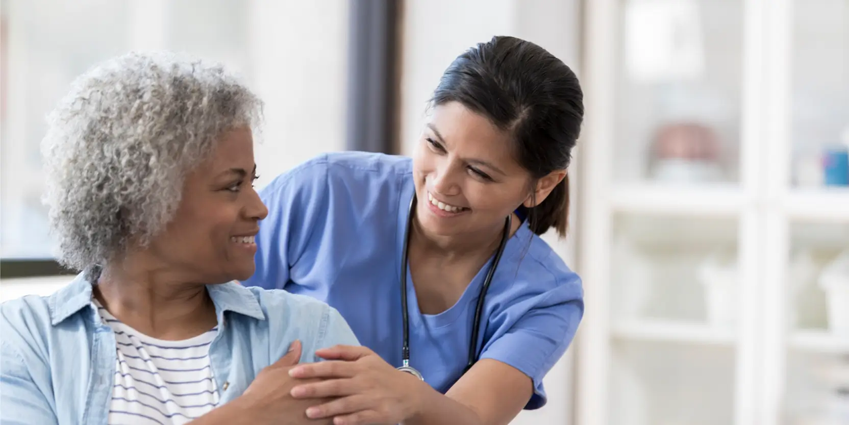 A smiling nurse stands beside an elderly woman, highlighting a moment of compassion and connection in healthcare.
