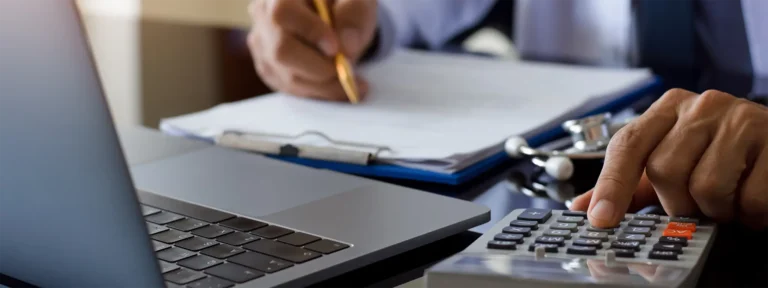 A man engages with a laptop, utilizing a calculator and pen for his work.