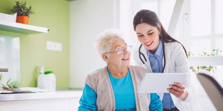 A healthcare professional with a stethoscope examines an elderly woman, demonstrating a patient-care interaction.