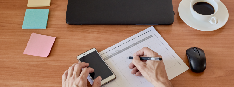 Writing on paper, with a smartphone and a cup of coffee nearby.