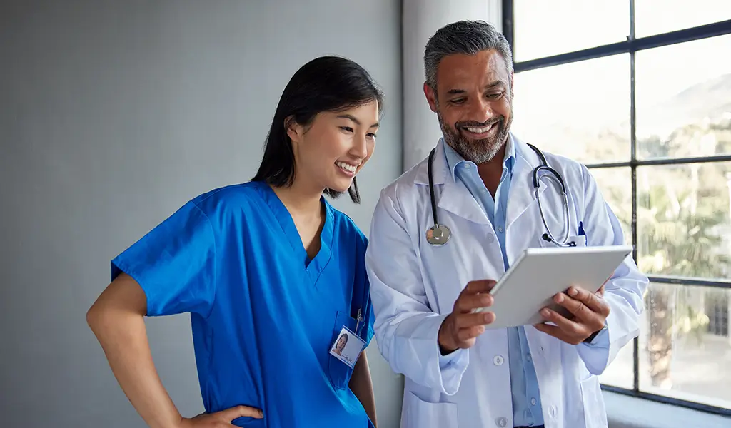 A doctor and patient reviewing information together on a tablet in a clinical setting.