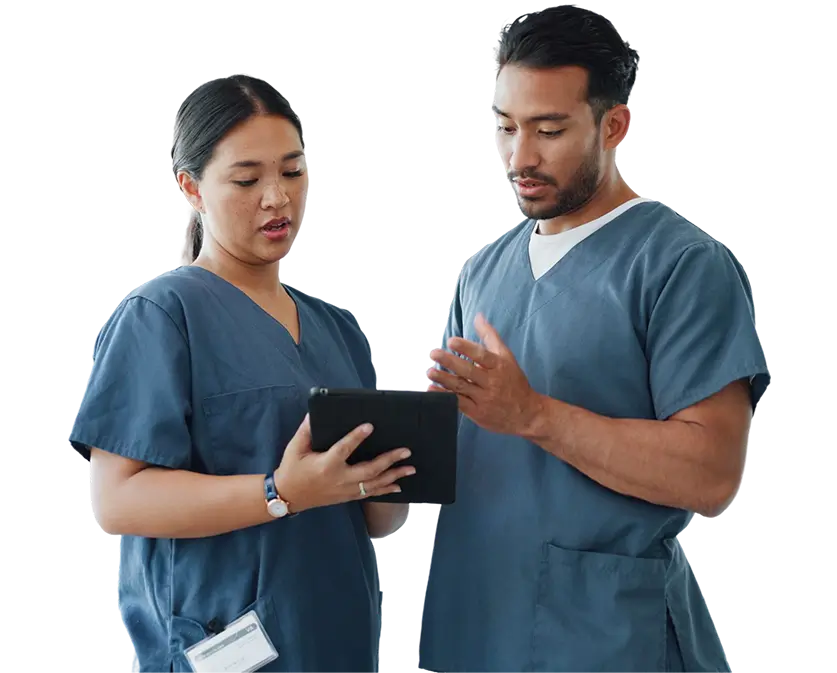 Two nurses dressed in scrubs examining a tablet, engaged in a discussion in a healthcare environment.